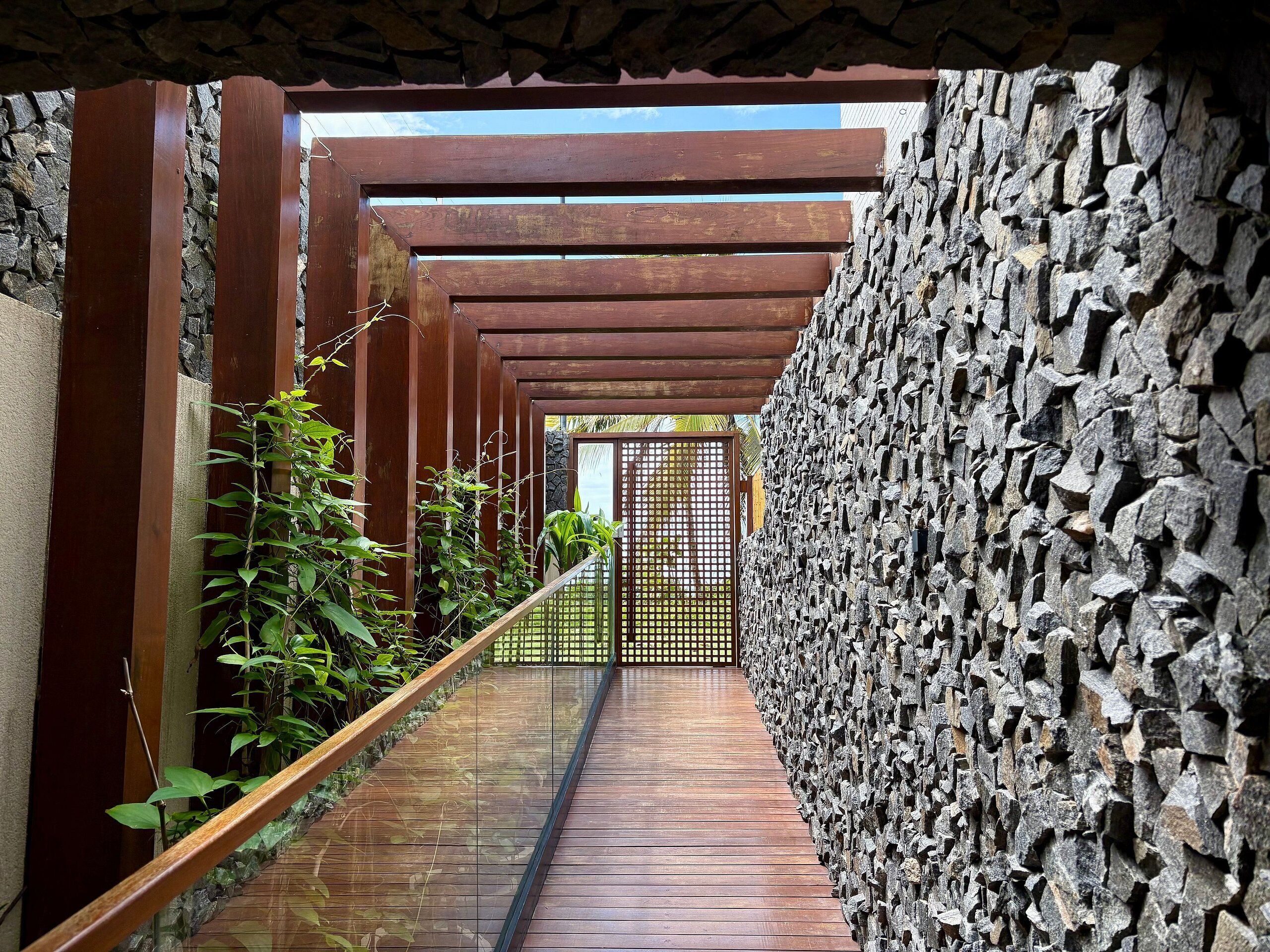 En træbro med en stenvæg på den ene side og en overdækket træpergola.
