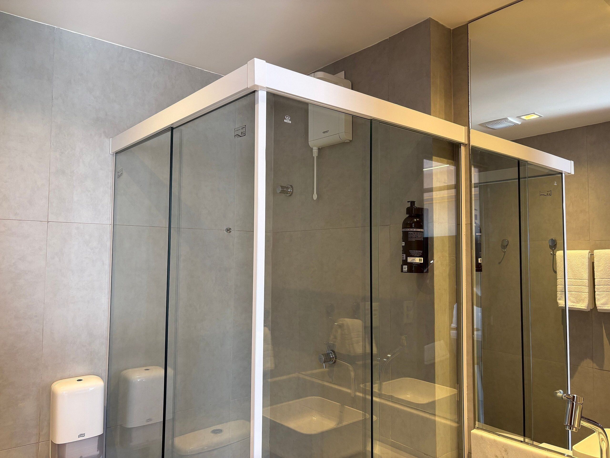 Un baño moderno con ducha envuelta en vidrio, un secador de manos y un perchero para toallas.