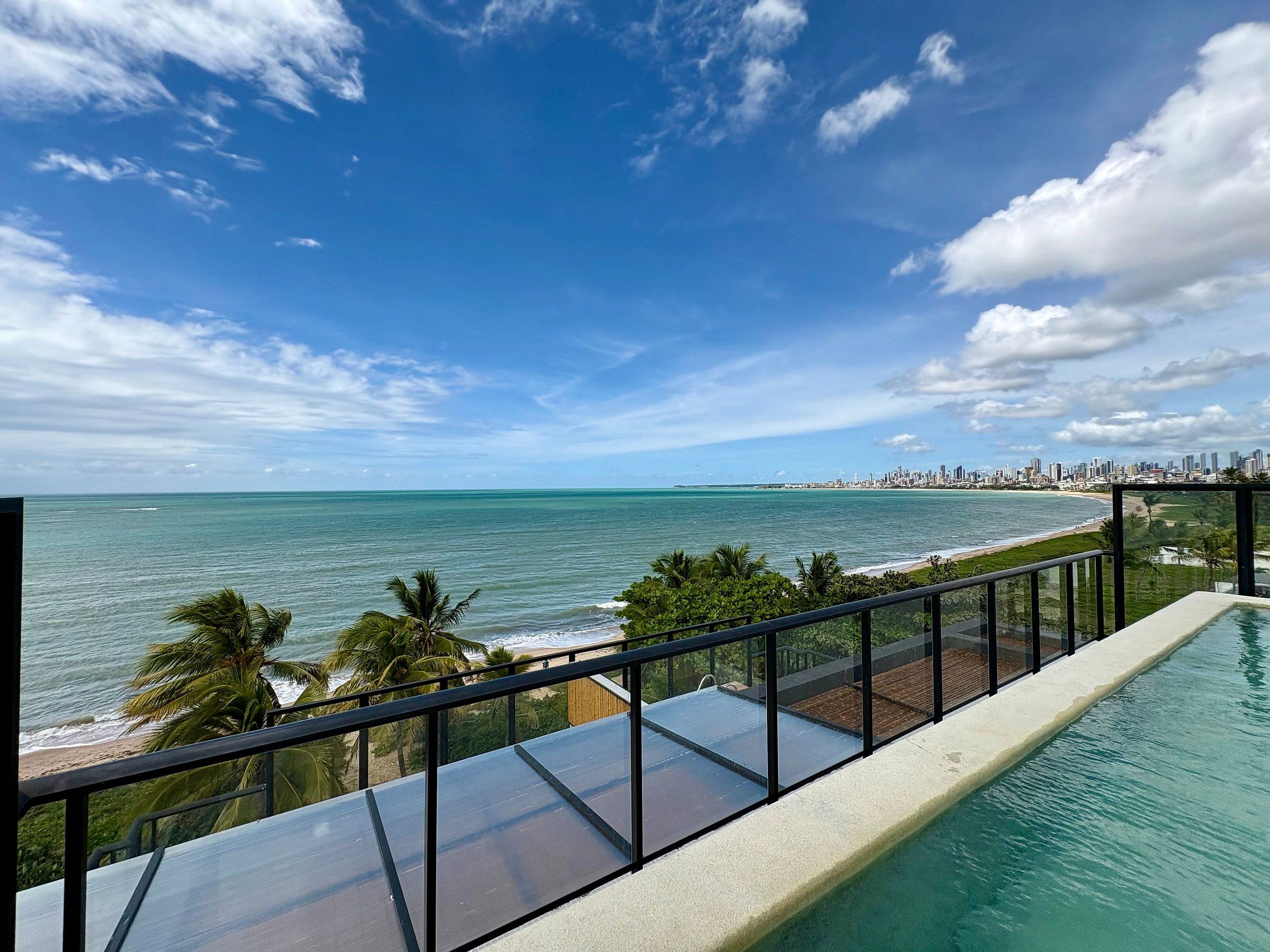 Piscina com vista clara do oceano e horizonte urbano ao longe.