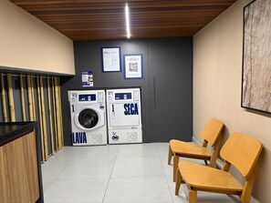 Un área de lavandería con dos lavadoras, un banco de madera y un código QR en la pared.