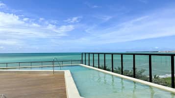 Ein Pool mit Blick auf das Meer, eine Holzterrasse und ein Metallgeländer.