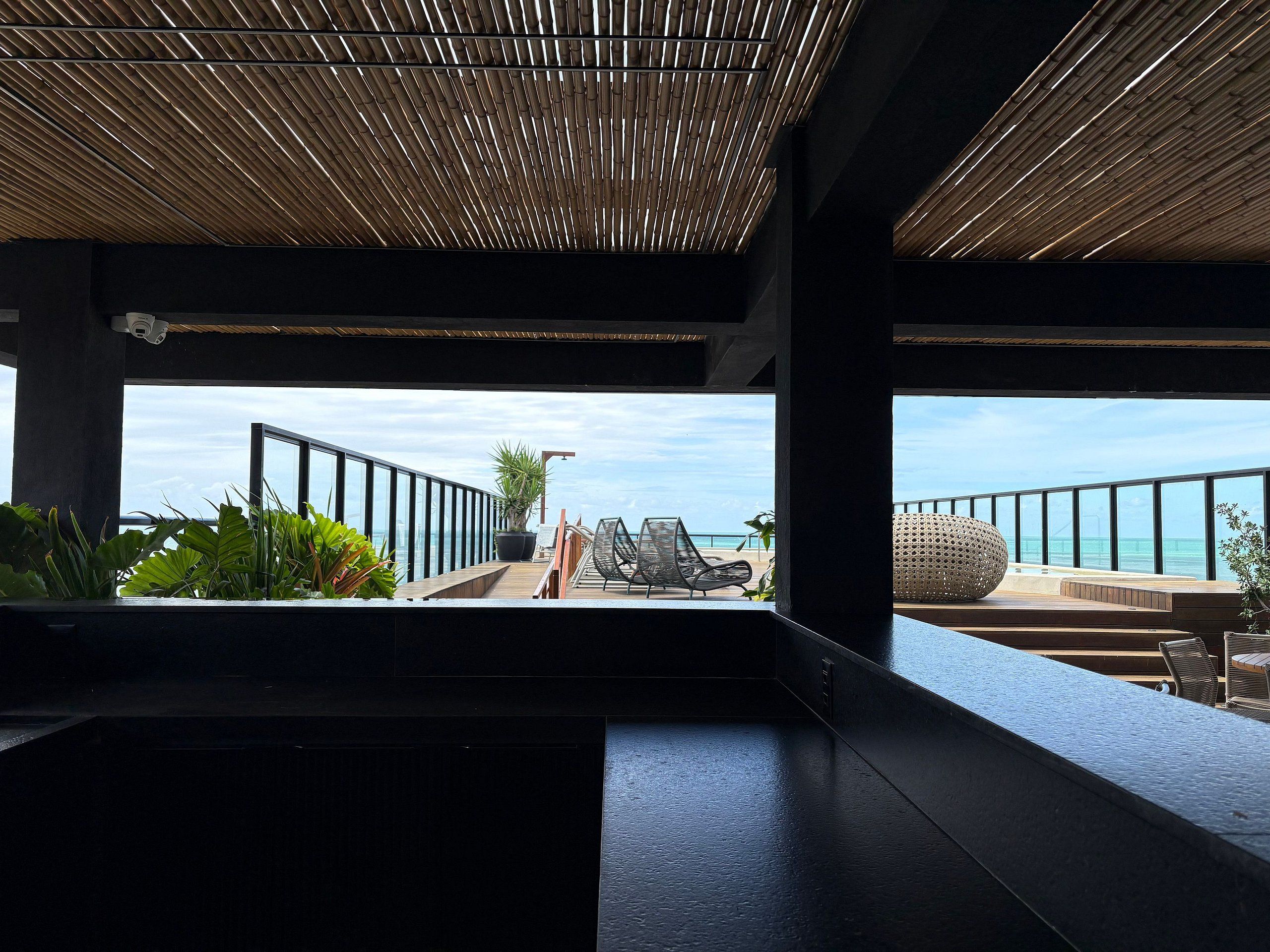 Un interior moderno con vista al océano, que presenta un techo de madera, una zona de estar con una mesa redonda y una planta en maceta.