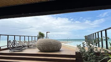 Een terras met lounge stoelen en een grote geweven plantenbak, met uitzicht op een helderblauwe lucht en een verre brug.