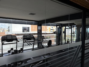 A gym with exercise equipment, large windows, and a view of the cityscape. - Refugio Sofisticado no Restinga (João Pessoa)