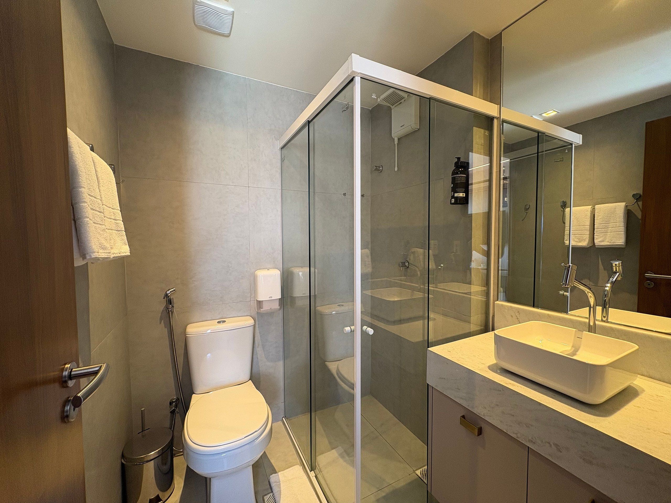 Un baño moderno con ducha de vidrio, inodoro y lavamanos con espejo.