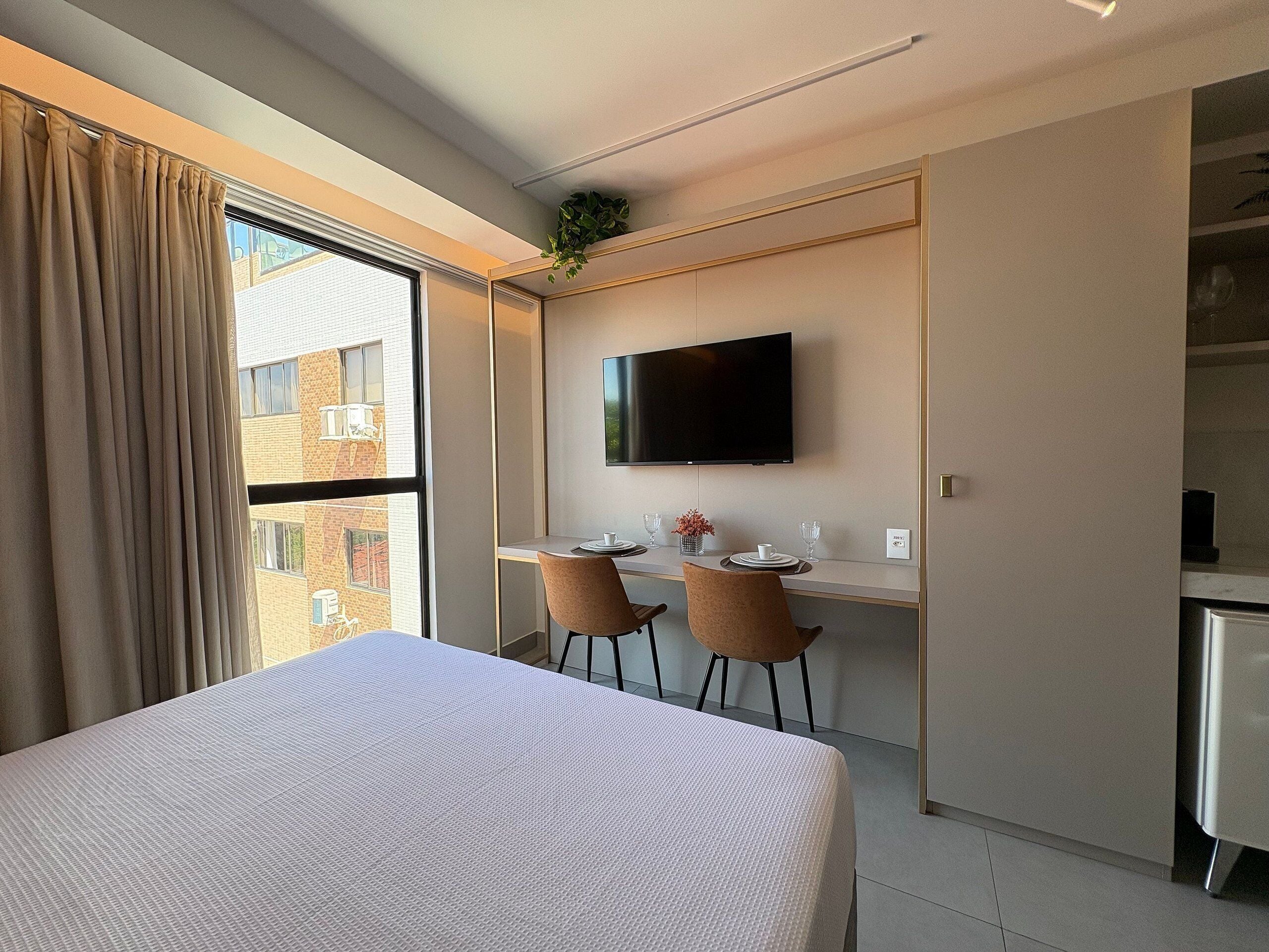 Une chambre d’hôtel comprenant un lit, un bureau avec deux chaises, une télévision et une vue sur les bâtiments environnants.