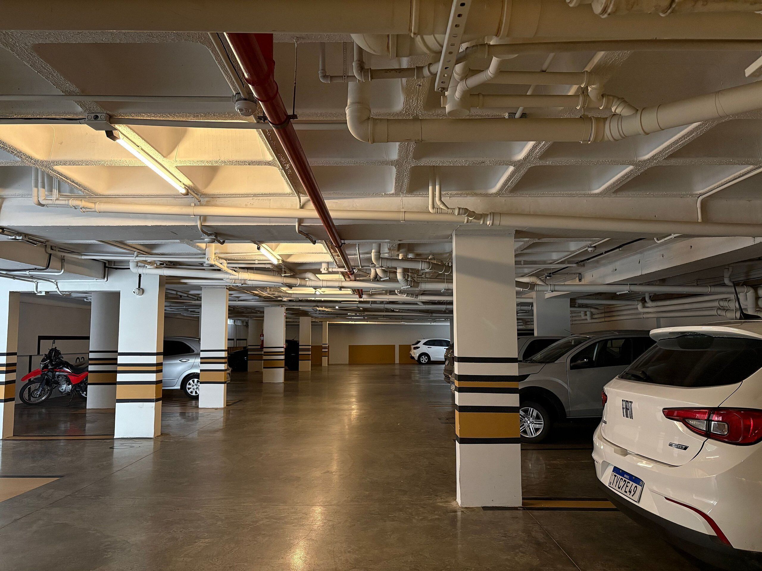 A multi-level parking garage with concrete pillars and overhead pipes.