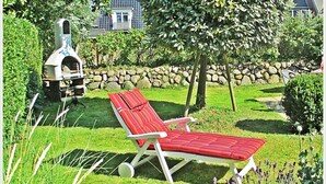 En have med en rød liggestol, en stenvæg og en grill.