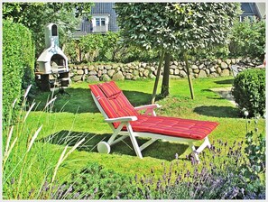 A garden with a red lounge chair, a stone wall, and a barbecue grill. - 4-Room Vacation Apartment "SYLTER DEICHWIESE" with Garden/Terrace in Westerland, Sylt (Sylt-Westerland)
