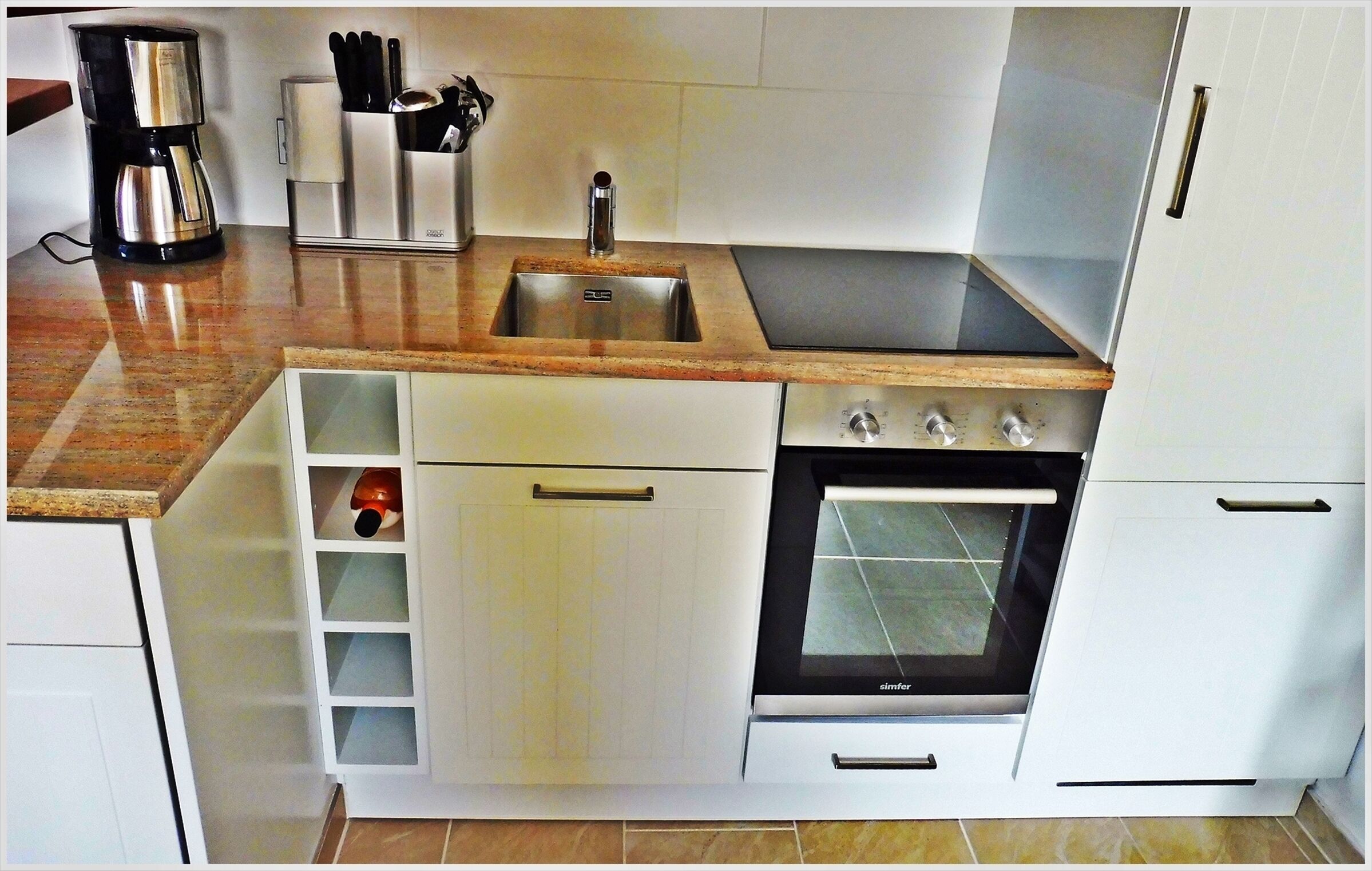 Eine kompakte Küche mit Spüle, Herd, Backofen und Kaffeemaschine.
