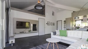 Una sala de estar moderna con una televisión de pantalla plana, un sofá blanco, una mesa de centro redonda y una alfombra gris.