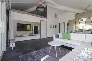 Ein modernes Wohnzimmer mit Flachbildfernseher, einem weißen Sofa, einem runden Couchtisch und einem grauen Teppich.