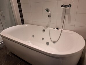 Eine freistehende, weiße Badewanne mit Handbrause und integriertem Wasserhahn.