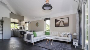 Una sala de estar moderna con un sofá blanco, una mesa de centro redonda y un tapete gris. Se ve una cocina al fondo con un comedor.