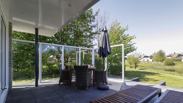 Un patio moderno al aire libre con cerramiento de vidrio, mobiliario de mimbre y un banco de madera.