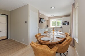 Ein Essbereich mit einem runden Holztisch und vier Stühlen, im Hintergrund eine Küche und ein Fenster mit Jalousien.