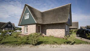 A single-story house with a steeply pitched roof, brick exterior, and a small front yard with shrubs. - Beach Villa With Garden & Water Access (Makkum)
