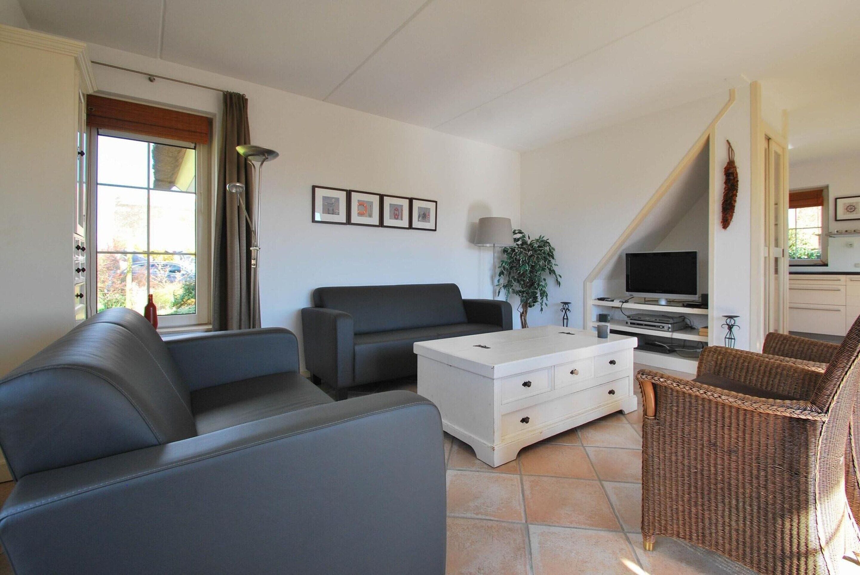 Una sala de estar con un sofá, un aparador blanco, un televisor y una silla de mimbre.