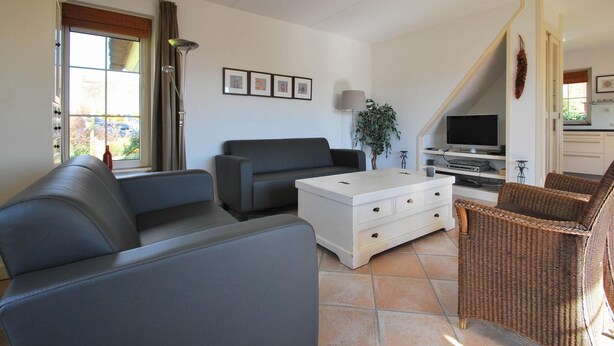 A living room with a sofa, a white chest of drawers, a television, and a wicker chair. - Beach Villa With Garden & Water Access (Makkum)