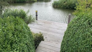 A wooden dock leading to a canal with houses in the background. - Beach Villa With Garden & Water Access (Makkum)
