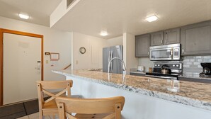 Une cuisine moderne dotée d’un plan de travail en marbre, d’appareils électroménagers en acier inoxydable et de chaises en bois.