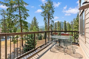 En balkon med et metalt bord og stole, med udsigt over et skovområde med bjerge i det fjerne.