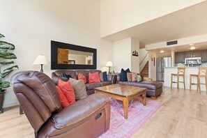 Ein modernes Wohnzimmer mit Ledersofas, einem Couchtisch und einer Küche im Hintergrund.
