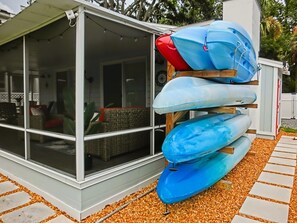 A covered outdoor area with a glass enclosure, a stack of kayaks, and a gravel path. - Just Us River Retreat (Weeki Wachee)