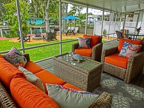An outdoor seating area with wicker furniture and orange cushions, overlooking a pool and greenery. - Just Us River Retreat (Weeki Wachee)