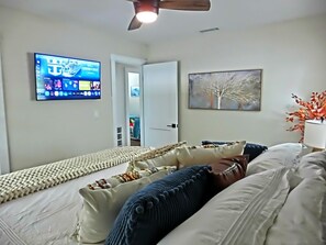 A bedroom with a bed, a television mounted on the wall, and a door leading to another room. - Just Us River Retreat (Weeki Wachee)