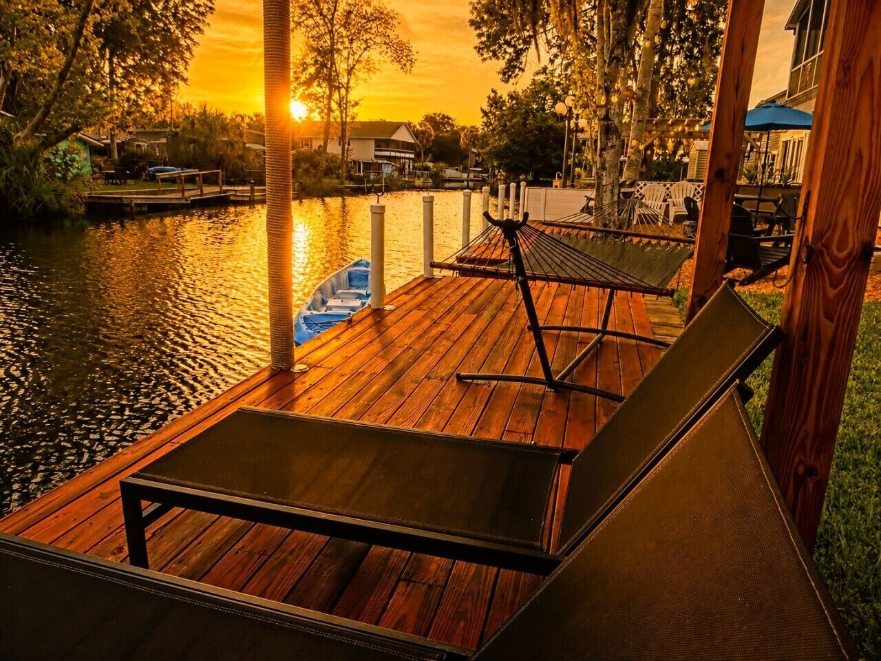 A wooden deck with lounge chairs and a boat docked by the water.