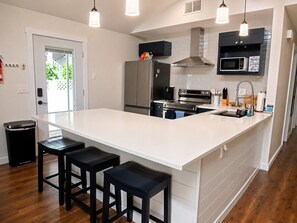 A modern kitchen with a large island, stainless steel appliances, and black bar stools. - Just Us River Retreat (Weeki Wachee)