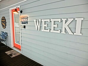 A wall with the word 'WEEKI' in large letters, a door with a red frame, a welcome mat, and a small sign above the door. - Just Us River Retreat (Weeki Wachee)
