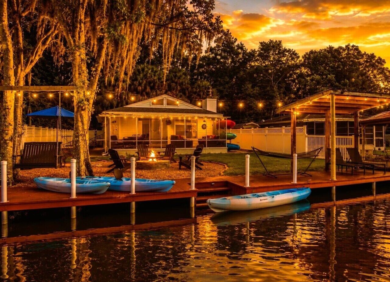 A waterfront property with a dock, kayaks, a covered seating area, and a building with string lights.
