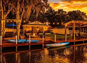 A waterfront property with a dock, kayaks, a covered seating area, and a building with string lights. - Just Us River Retreat (Weeki Wachee)