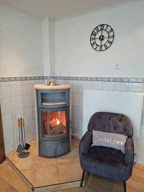 A room with a stone fireplace, a clock on the wall, and a plush armchair with a cushion.