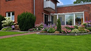 A modern brick house with a glass conservatory, surrounded by a well-maintained garden with various flowers and a lawn. - A hidden gem in the Emsland region: the "Ferienglück" vacation rental—spacious, ground-floor, bright, and idyllic. (Meppen)