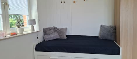 A bedroom with a bed, a window with blinds, a bedside table with a lamp, and a wall-mounted decoration.