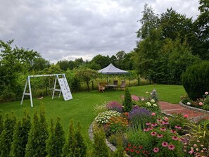 A garden with a swing set, a gazebo, and a variety of flowers.