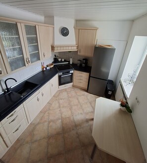 A kitchen with a black countertop, a stainless steel refrigerator, and a clock on the wall.
