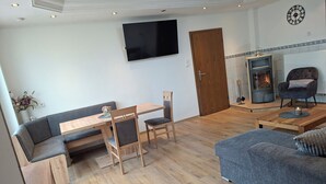 A modern living room with a wooden dining table, two chairs, a grey sofa, a television mounted on the wall, and a fireplace. - A hidden gem in the Emsland region: the "Ferienglück" vacation rental—spacious, ground-floor, bright, and idyllic. (Meppen)