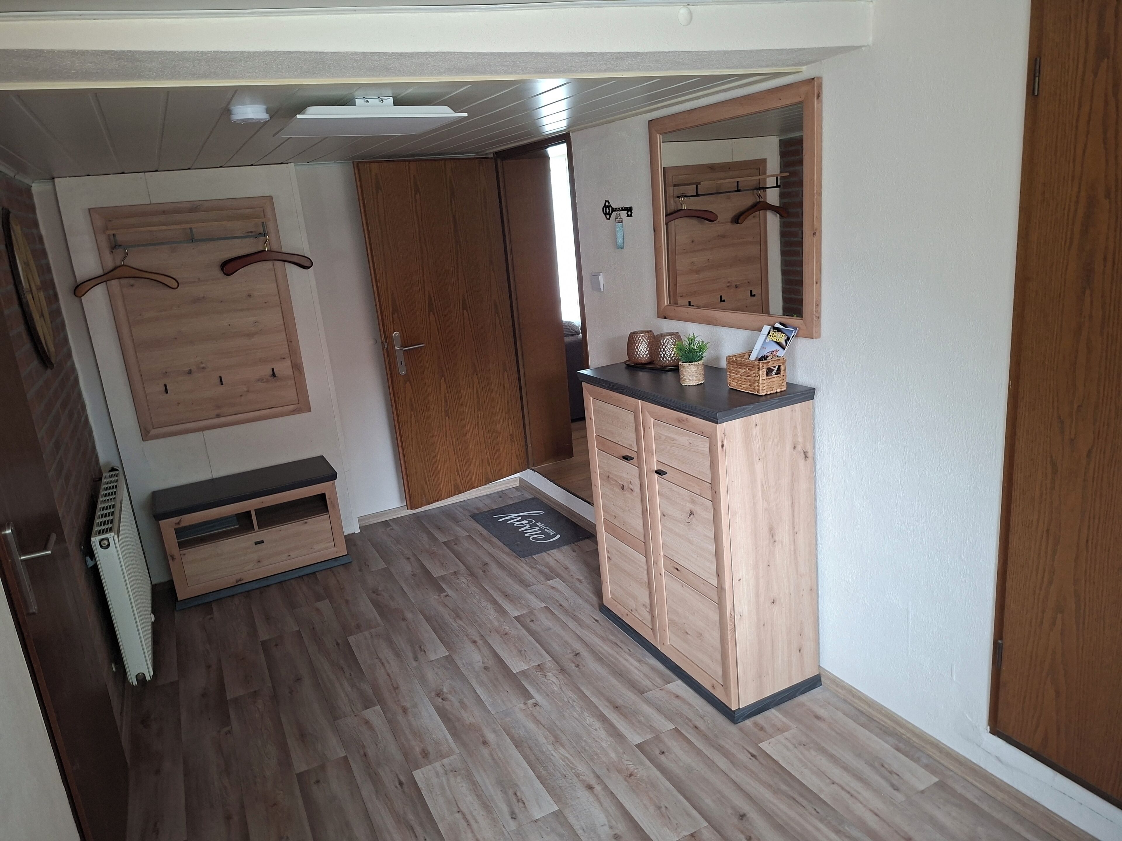 A hallway with wooden flooring, a bench, a wardrobe, and a mirror.