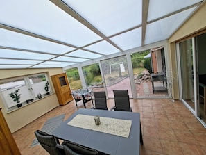 A conservatory with a table and chairs, a wooden cabinet, and a view of the garden.