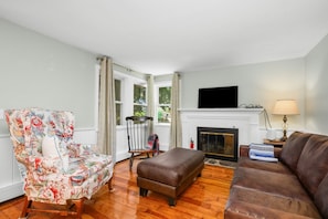 A living room with a fireplace, a television mounted above it, and a sofa. - Recently Renovated, Centrally Located Yarmouth Cottage (Yarmouth)