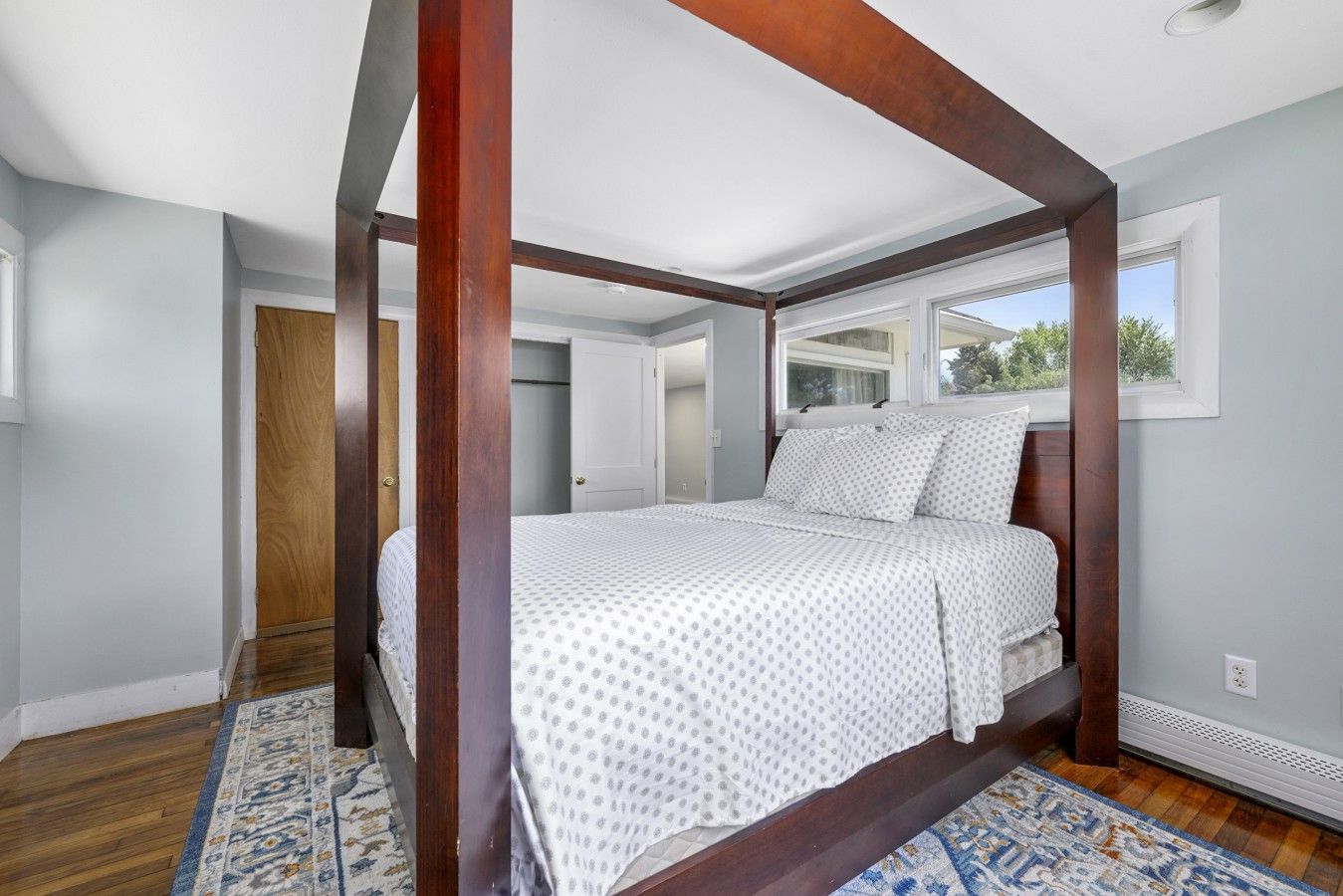 A four-poster bed in a bedroom with a view of the outdoors through a window.