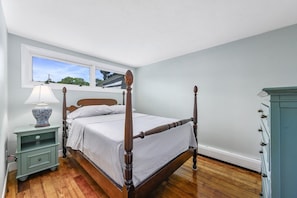 Ein Schlafzimmer mit Himmelbett, Nachttisch mit Lampe, Kommode und Fenster mit Blick.