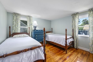Une pièce avec deux lits en bois, une commode bleue et une fenêtre avec des rideaux.