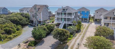 A coastal residential area with multi-story houses, a gravel driveway, and a clear view of the ocean.