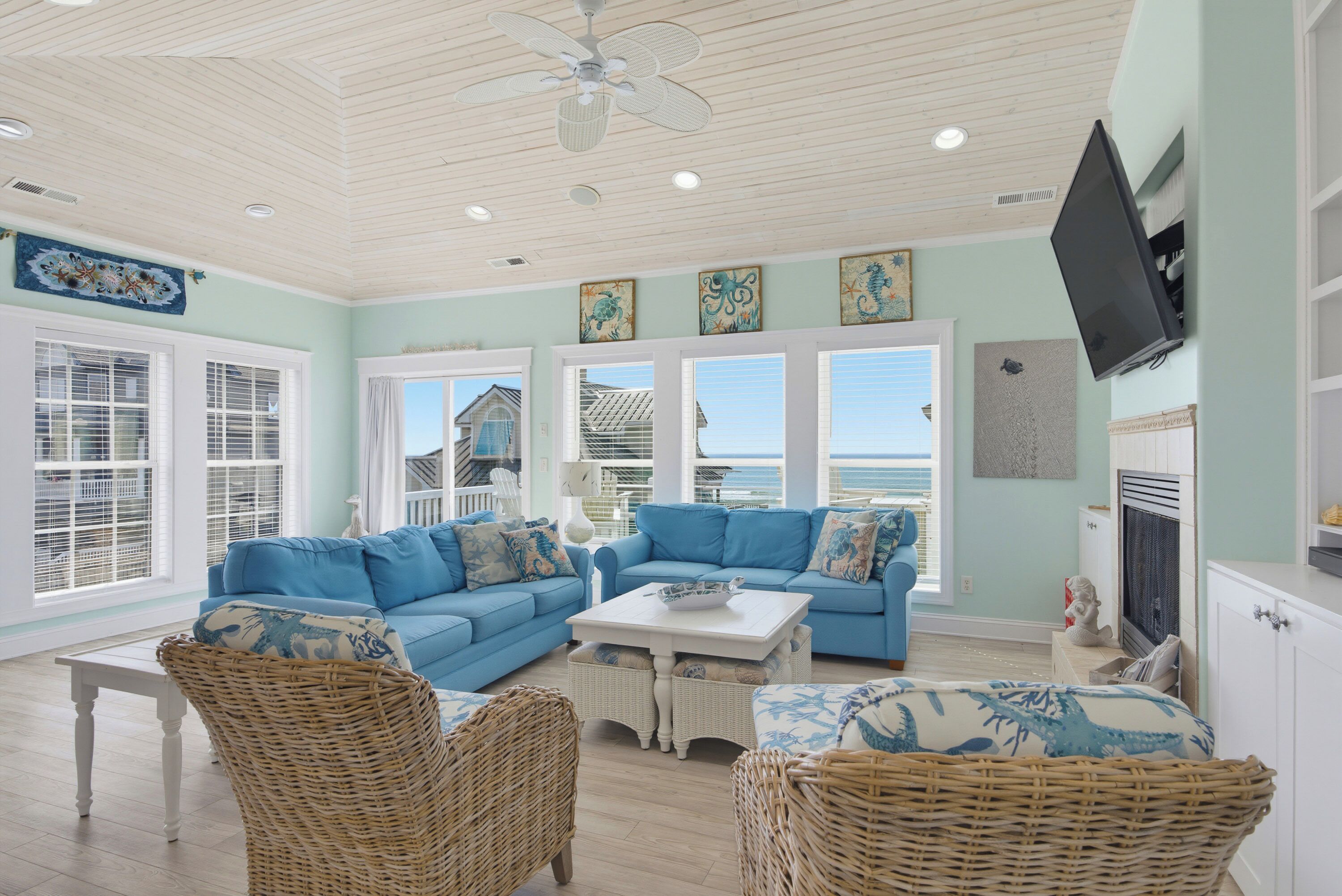 A spacious living room with a large blue sofa, wicker chairs, and a ceiling fan.