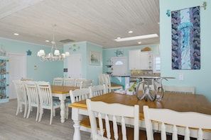 A dining area with a wooden table and white chairs, a chandelier, and nautical-themed wall art. - Oceanfront with hot tub and elevator (North Topsail Beach)
